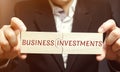 Businessman collects wooden puzzles with the words business investments. Increase capital. Investing your assets in your own or Royalty Free Stock Photo