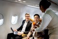 Businessman in comfortable seat inside airplane, female cabin crew air hostess serving orange juice drink, flight attendant take Royalty Free Stock Photo