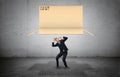 Businessman on concrete background cowering below a large open carton box falling on him.