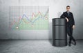 Businessman in confident pose standing next to oil barrel on background of graph