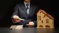 Businessman counts a money stack near a house model on a table