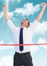 Businessman crossing finish line with arms up against sky and cloud Royalty Free Stock Photo