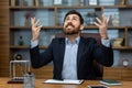 Businessman in despair at workplace raised hands and head up, upset man inside office in jacket, upset boss Royalty Free Stock Photo