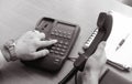 The businessman dials the number on the landline phone, holds the handset in his right hand