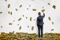 A businessman draws many golden dollar coins flying in a huge pile on a white wall.