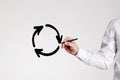 Businessman draws a recycling circle with arrows on gray background. Business or economic stagnation or recycle