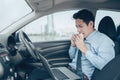 Businessman eating sandwich while working in laptop in the drivers seat in his car. Busy businessman and food in car