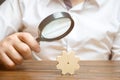 Businessman examines a wooden gear through a magnifying glass. study and analysis of business processes and subjects.