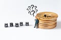 Businessman figurine with question marks above his head looking at cubes with plans text while leaning to bitcoin stack