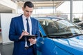 Businessman fills in documents on car at car dealership Royalty Free Stock Photo