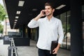 Businessman with folder talking on cell phone near business center