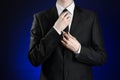 Businessman and gesture topic: a man in a black suit and white shirt correcting a jacket and tie on a dark blue background in stud