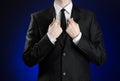 Businessman and gesture topic: a man in a black suit and white shirt correcting a jacket and tie on a dark blue background in stud