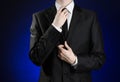 Businessman and gesture topic: a man in a black suit and white shirt correcting a jacket and tie on a dark blue background in stud