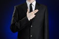 Businessman and gesture topic: a man in a black suit and white shirt, put his hand on his chest as a sign of a pistol on a dark bl Royalty Free Stock Photo