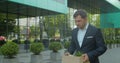 Businessman gets fired and walking near office center with carton box and documents with a table flower. Lost His Job Royalty Free Stock Photo