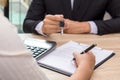 Businessman giving house keys and customer signing loan agreement document with calculator on wooden desk.