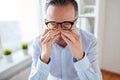 Businessman in glasses rubbing eyes at office