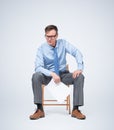 Businessman in glasses, a shirt and tie sits on a chair holding paper in his hands, on light blue background.