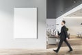 Businessman goes to blank white poster on light grey wall in modern open space office with light furniture and wooden floor Royalty Free Stock Photo
