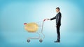 A businessman grabs a metal shopping cart with a huge golden egg stored inside. Royalty Free Stock Photo