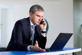 Businessman gray in a suit talking on the phone in front of laptop.