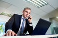 Businessman gray in a suit talking on the phone in front of laptop.