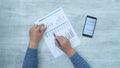 Businessman hand checking reported profits on paper and smartphone.