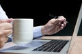 Businessman hand holding coffee cup and pen to display laptop on table Royalty Free Stock Photo