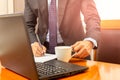 Businessman hand holding coffee cup and writing on notebook on wprking desk. Royalty Free Stock Photo