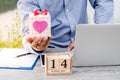 Businessman hand holding gift box with 14 February wooden calendar and laptop. Valentine day concept Royalty Free Stock Photo