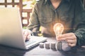 Businessman hand holding lightbulb on stack coins, and working with computer on workplace. Creative ideas concept of saving money Royalty Free Stock Photo