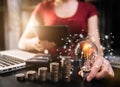 Businessman hand holding lightbulb with using laptop computer and money stack in office. Royalty Free Stock Photo