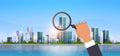 Businessman hand holding magnifying glass search concept over big modern city building skyscraper cityscape background Royalty Free Stock Photo