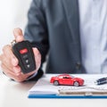 Businessman hand holding remote keyless with car toy, pen and contract document. buy and sale, insurance, rental and contract