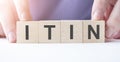 Businessman hand holding wooden cube block with ITIN business word on table background