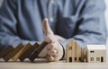 Businessman hand protect and stop wooden house from domino falling wooden bar for risk management and analysis of real estate Royalty Free Stock Photo