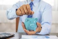 Businessman hand putting coin into blue piggy bank, saving money for future investment plan and retirement fund concept Royalty Free Stock Photo