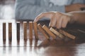 Businessman hand stopping falling wooden dominoes effect from continuous toppled or risk, strategy and successful intervention Royalty Free Stock Photo