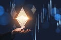 Businessman hand in suit holding hologram icon of ethereum cryptocurrency. Financial graph and candlestick financial chart.