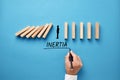 Businessman hand writing the word inertia with silhouette of a man standing against collapsing wooden dominos. Business inaction,