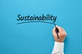 Businessman hand writing the word sustainability on blue background. Corporate environmental ecology strategy in business Royalty Free Stock Photo