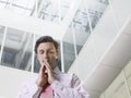 Businessman With Hands Clasped In Office Atrium