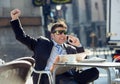 Businessman having breakfast coffee reading newspaper talking happy on mobile phone doing victory sign Royalty Free Stock Photo