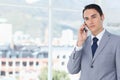 Man in his 30s standing by window in office, light-gray suit navy-tie, holding phone, copy space Royalty Free Stock Photo