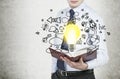 Businessman is holding a book with flying around business icons and a light bulb as a concept of the new business ideas. Royalty Free Stock Photo