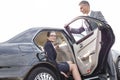 Businessman holding car door for colleague against sky