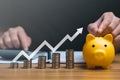 Businessman holding a coin in a piggy bank with graphs and arrows showing charts on his desk. Royalty Free Stock Photo