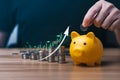 Businessman holding a coin in a piggy bank with graphs and arrows showing charts on his desk. Royalty Free Stock Photo