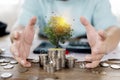 A businessman holding a coin with a tree that grows and a tree that grows on a pile of money. The idea of maximizing the profit